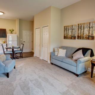 A cozy living room with a light blue sofa, armchair, and carpeted flooring, connected to a dining and kitchen area.