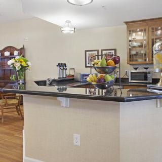 A modern kitchen with a sleek countertop, fruit bowl, and flowers, adjacent to a dining area.