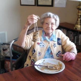 An elderly woman smiling and holding up a keychain while sitting at a table indoors.