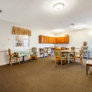 A dining area with tables and chairs, featuring wood cabinets and carpeted flooring.
