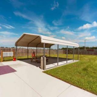A covered picnic area with benches in a fenced park on a sunny day.
