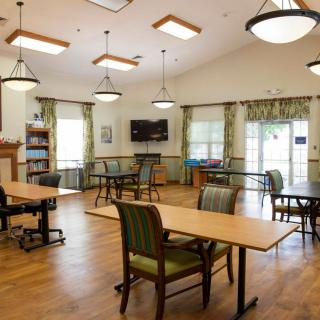 A well-lit communal room with tables, chairs, and a television.
