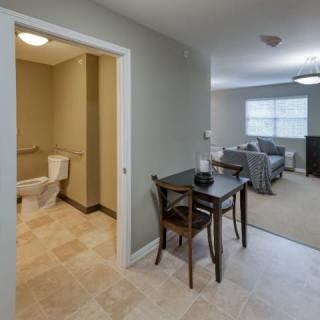A cozy apartment interior featuring a small dining area, adjacent bathroom, and a living room.