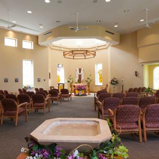 An interior view of a church featuring an altar, pews, and floral decorations.