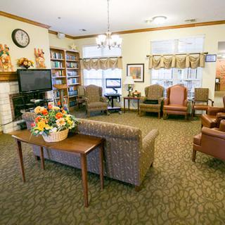 A cozy living room with comfortable seating, a television, bookshelves, and floral decorations.