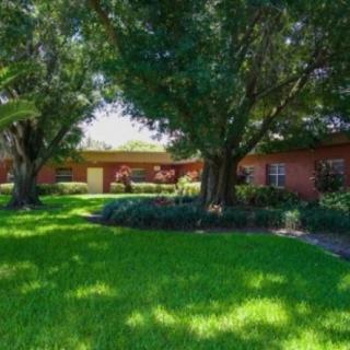 A quaint brick house surrounded by lush green grass and large trees.