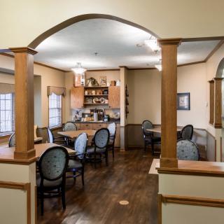 A cozy dining area with a view into an adjoining kitchen, featuring traditional decor and wooden furniture.