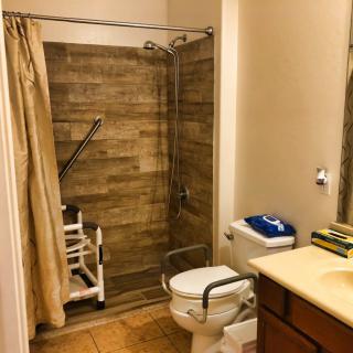 An accessible bathroom with a shower area, equipped with grab bars and a shower chair.