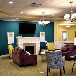 A cozy living room with colorful armchairs and a fireplace, featuring a mounted television and elegant chandeliers.