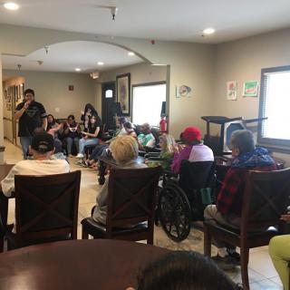 A group of people gathered indoors, listening to a speaker.
