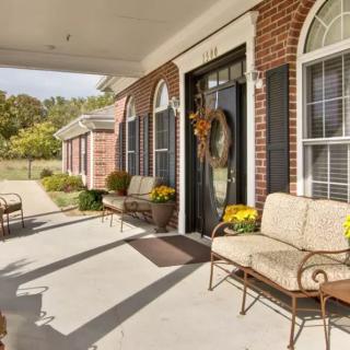 A cozy porch with outdoor seating and floral decorations at the entrance of a brick house.