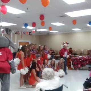 A lively celebration featuring cheerleaders and a mascot, captured during an event decorated with colorful balloons.