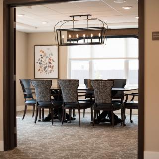 A well-lit conference room with a large table and chairs, featuring a modern chandelier.