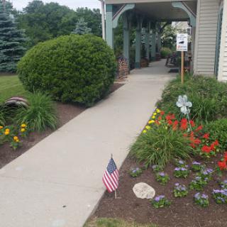 A well-maintained pathway lined with vibrant flowers and an American flag, leading to the entrance of a building.