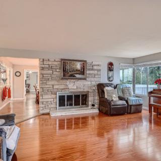 A cozy living room with a stone fireplace, hardwood floors, and large windows providing ample natural light.
