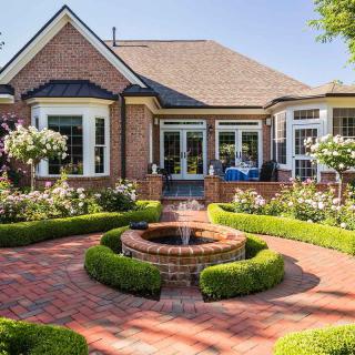 A beautiful house with a brick exterior, surrounded by a lush garden featuring a central fountain and well-maintained hedges.
