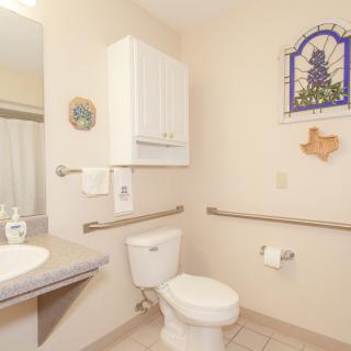 A clean and accessible bathroom with a toilet, sink, and handrails.
