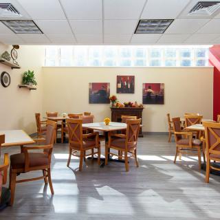 A cozy cafe interior with wooden tables and chairs, decorated with wall art and plants under natural lighting.