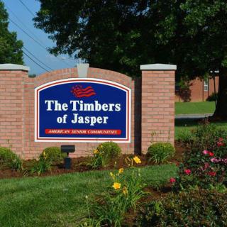 A sign for 'The Timbers of Jasper' set in a landscaped garden with flowers and brick columns.