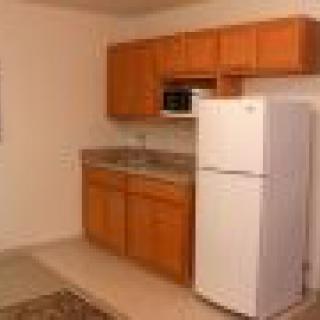 A compact kitchen with wooden cabinets, a countertop, and essential appliances including a fridge and microwave.