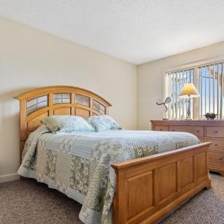 A cozy bedroom featuring a wooden bed frame, matching dresser, and a window letting in natural light.