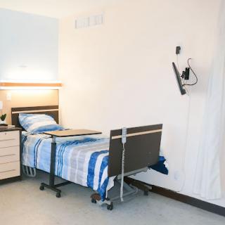 A well-lit hospital room featuring a patient bed with blue bedding and nearby furniture.