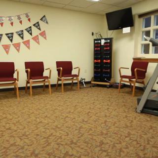 An empty waiting room with chairs, a TV screen, and a treadmill.