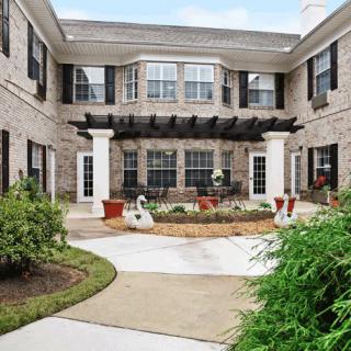 A landscaped courtyard with a pathway surrounded by shrubs and a two-story brick building.