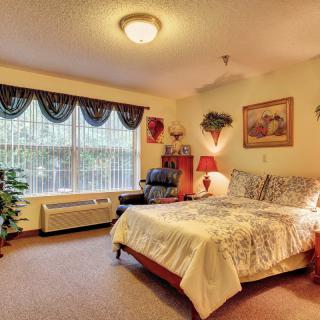 A cozy bedroom decorated with warm tones and featuring a large window, a bed with patterned bedding, and various decorative elements.