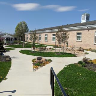 A well-maintained pathway winds through a landscaped area in front of a school building on a sunny day.
