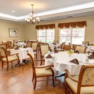 An elegant dining room with neatly arranged tables and chairs, featuring chandeliers and large windows.