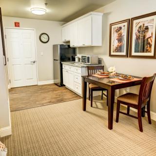 A modern kitchen and dining area featuring a compact kitchenette, a wooden table with two chairs, and framed artwork on the walls.