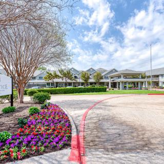 A landscaped garden with colorful flowers leads to a large building under a partly cloudy sky.
