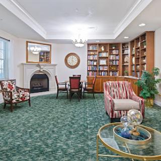 A cozy living room featuring a fireplace, bookshelves filled with books, and comfortable seating on green carpet.