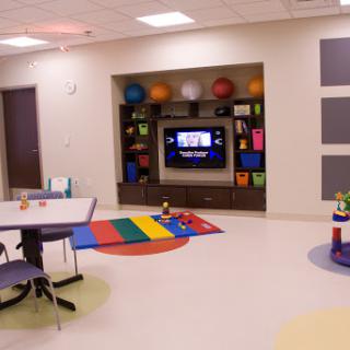 A vibrant playroom designed for children, featuring a TV, colorful rugs, and various exercise balls.