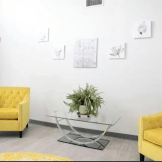 A modern living room with vibrant yellow armchairs, a sleek glass table, and minimalist wall art.