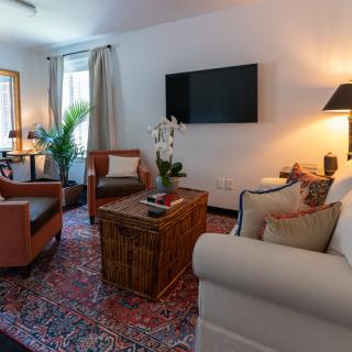 A cozy living room with modern decor, featuring a comfortable sofa, armchairs, a woven coffee table, and a large TV mounted on the wall.