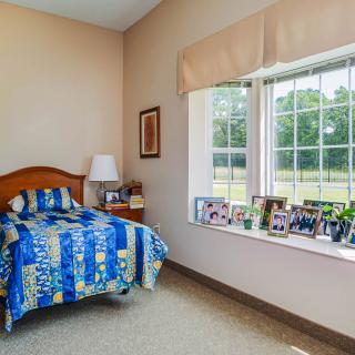 A cozy bedroom with a single bed featuring colorful bedding, a window seat adorned with decorative items and photos, and soft natural light.