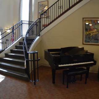 A grand piano sits beside a winding staircase in a well-lit interior space adorned with artwork.