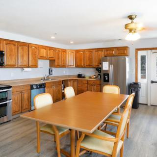 A spacious kitchen with wooden cabinets and a dining table set, equipped with modern appliances and a ceiling fan.