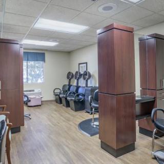 A spacious salon interior featuring chairs, hair dryers, and wood flooring.