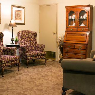 A cozy living room with patterned armchairs, a wooden cabinet, and a lamp.