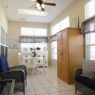 A bright living space with a seating area, dining table, and cabinet under large windows and a ceiling fan.
