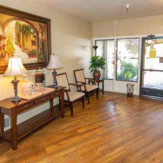 A well-lit lobby area with wooden flooring, featuring chairs, a console table with lamps, and decorative artwork.