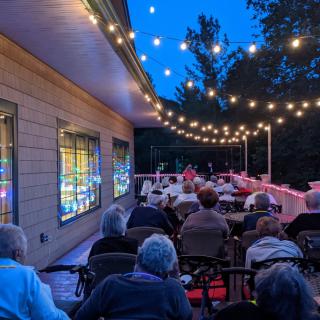 An outdoor evening gathering with people seated under string lights.