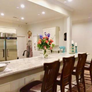 A modern kitchen with a marble counter, wooden stools, and a bouquet of colorful flowers.