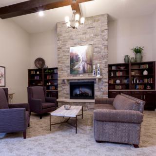 A cozy living room featuring a stone fireplace, armchairs, and bookshelves.