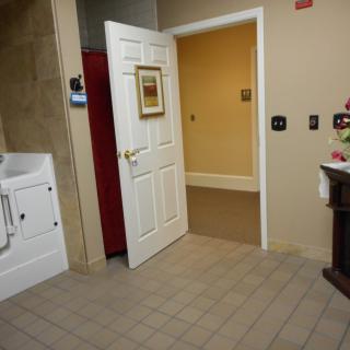An open door leading to a warmly lit hallway from a tiled room with a sink and wall decor.
