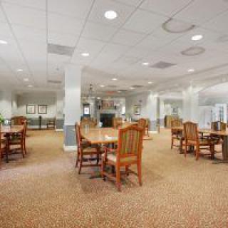 A spacious dining area with wooden tables and chairs, featuring soft lighting and carpeted flooring.