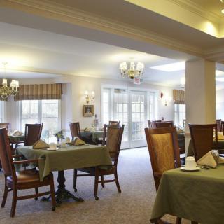 A well-lit dining area with neatly arranged tables and chairs, featuring elegant chandeliers and large windows.